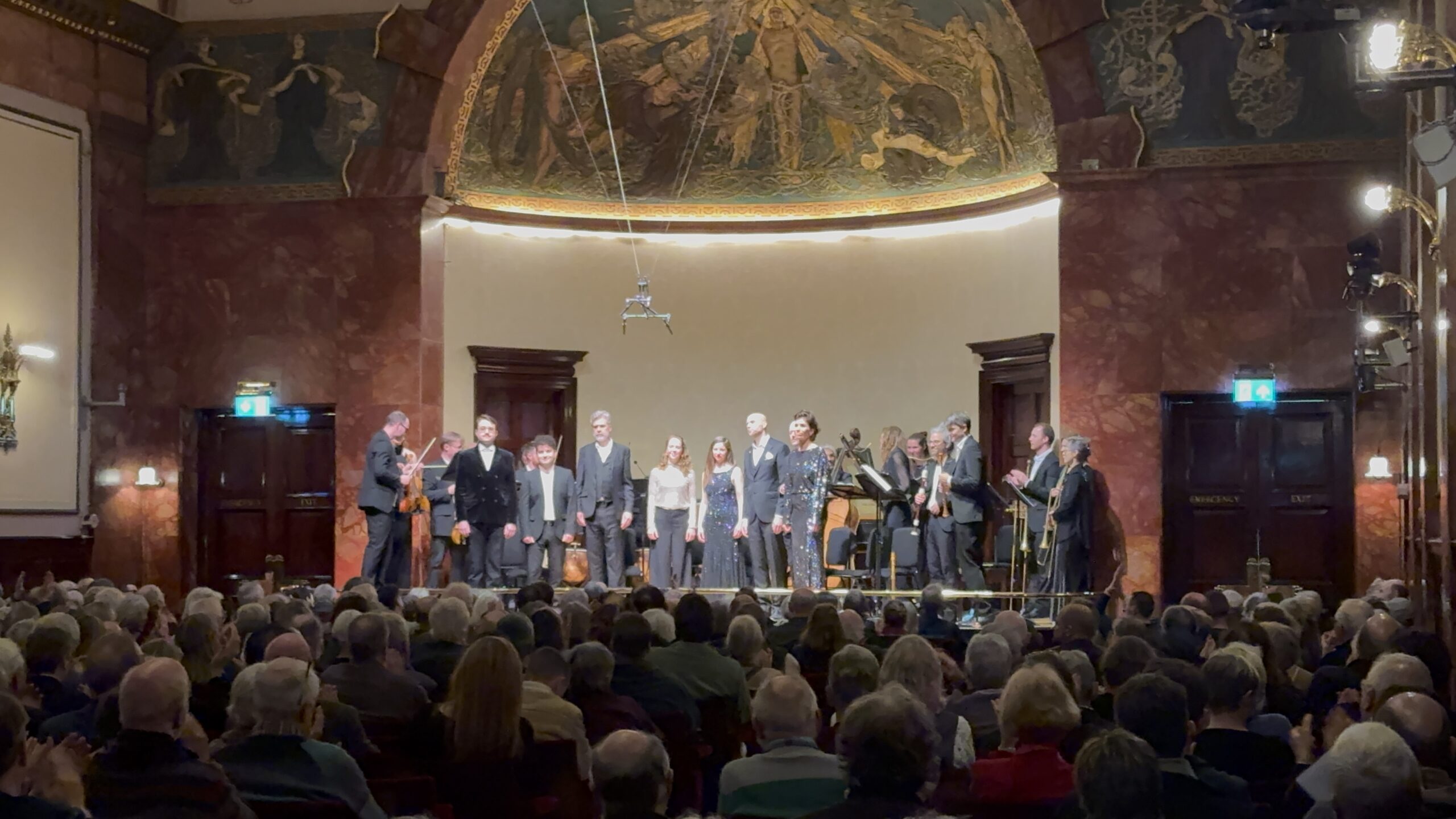 Concert hall stage with a choir and musicians performing before a large audience.